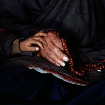 Un grand pere prie en egrenant son chapelet use aux cotes de son petit-fils (BHOUTAN) / A grandfather prays while fingering his worn rosary, a child's hand placed on his own (Bhutan)